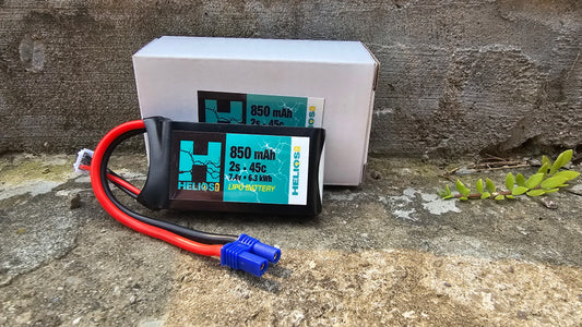 A 2S 850 MAH 45C LIPO battery with a blue label, connected to a red and black wire, placed on a stone surface.