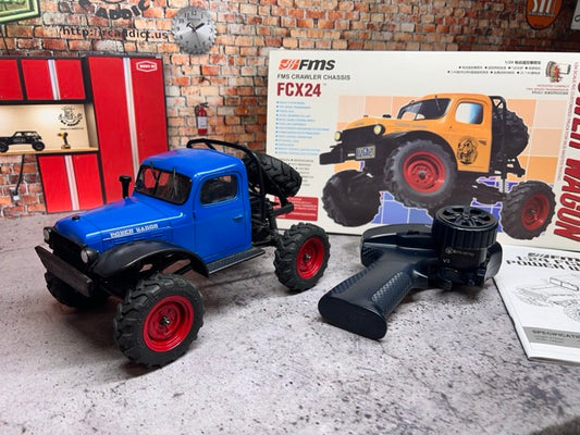 Blue FCX24 Power Wagon with red wheels on a surface next to a branded box and paper. -1