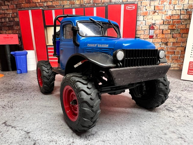 Blue off-road FCX24 Power Wagon with large black tires in a garage setting -1