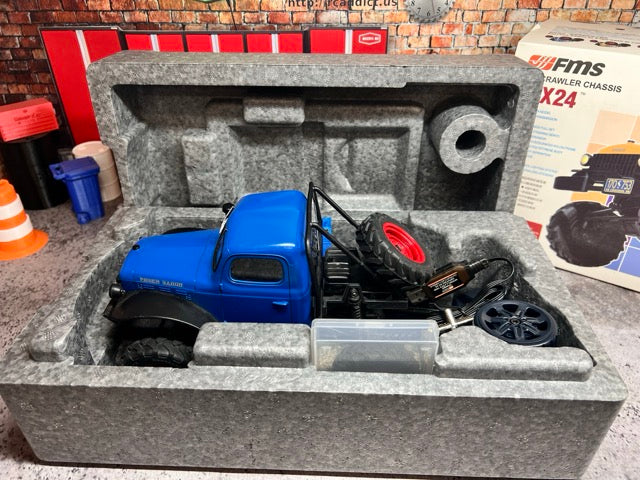 Blue FCX24 Power Wagon in a gray foam packaging with construction-themed items in the background. -1
