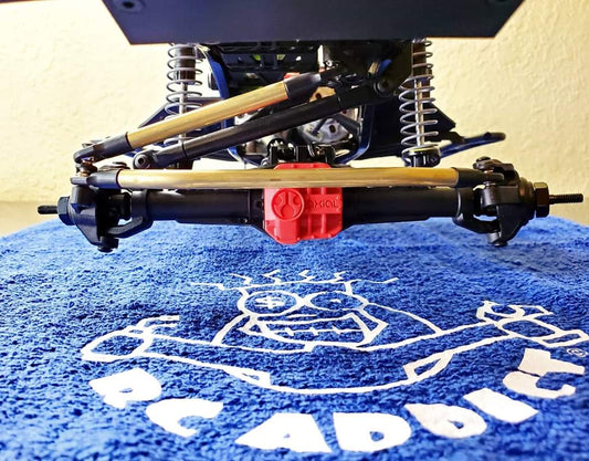 A brass steering link kit installed on a model vehicle, featuring high clearance links and a drag link, set against a blue backdrop with a white graphic.