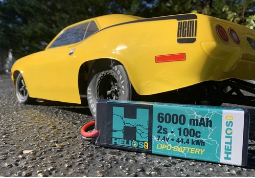A high-performance yellow remote control car with a detailed close-up of a Helios 2S 6000 mAh 100C Racing Lipo battery pack.
