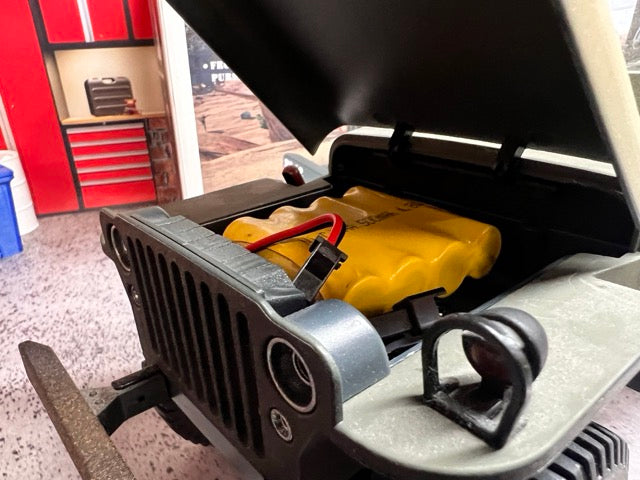 Close-up of a Willys MB Jeep open hood with a battery visible, set against a garage background. -2